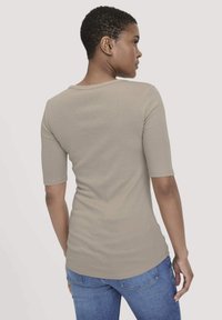 Strakke beige t-shirt met korte mouwen, ronde halslijn en een gladde textuur, gecombineerd met blauwe denim jeans in een staande pose.