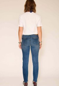 Jean en denim bleu cintré avec une taille mi-haute, deux poches arrière et une texture lisse, associé à un t-shirt blanc à manches courtes.