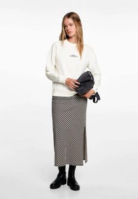 Cream sweatshirt with text, paired with a black and white patterned midi skirt featuring a side slit, and chunky black ankle boots.