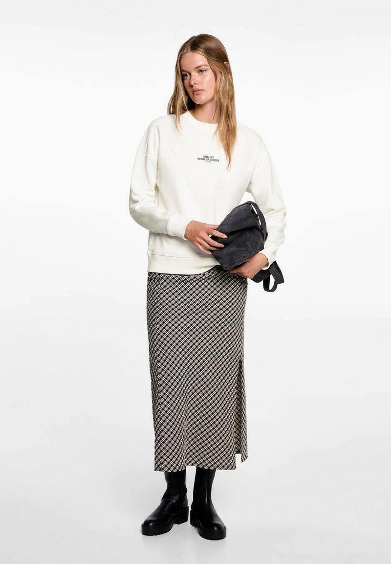Cream sweatshirt with text, paired with a black and white patterned midi skirt featuring a side slit, and chunky black ankle boots.