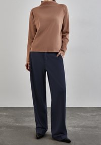 Brun långärmad topp med hög krage. Matchas med vida navybyxor och svarta pumps med spetsig tå. Slät tyg, avslappnad passform.