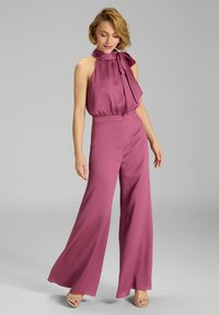 Paarse mouwloze jumpsuit met een halternek en strikdetail op de schouder. Brede broekspijpen en een gestructureerde stof.