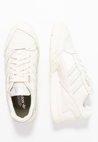 Baskets blanches en cuir et en matériau synthétique, avec un design bas, des accents gris subtils et trois rayures sur les côtés.