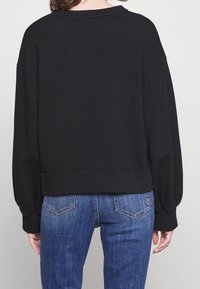 Pullover nero, oversize, con collo a giro e spalle scese, caratterizzato da una texture liscia e un orlo corto, abbinato a jeans blu.
