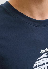 Camiseta de algodón azul marino con cuello redondo, que presenta un estampado gráfico blanco con el texto "Jack" y un diseño estilizado debajo del texto.