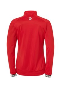 Rød sportsjakke med høj krave, lavet af glat stof. Har lange ærmer og et sort bånd med "Kemp" ved manchetterne.