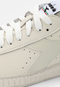 Baskets blanches en cuir avec un panneau latéral texturé, des accents gris et des lacets blancs. Présente des perçages et une semelle en caoutchouc à motif.