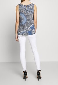 Blå mönstrad ärmlös topp med rund halsringning, med intrikata paisleymönster. Matchad med vita skinny jeans och svarta klackar.