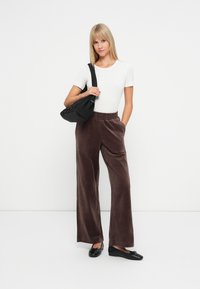 Brūni samta platā kāju bikses ar elastīgu jostu, savienotas ar pieguļošu balto īsām piedurknēm topu un melnajām baleta kurpēm, kopā ar melnu somu.