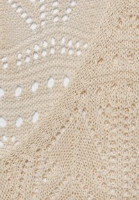 Tessuto all'uncinetto beige con motivi aperti e texture, caratterizzato da motivi a diamante e ovale, che conferiscono un aspetto leggero e arioso.