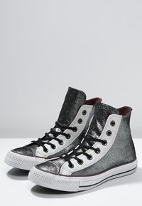 Vysoké tenisky s třpytivým stříbrným povrchem, bílými akcenty, černými tkaničkami a gumovými podrážkami. Disponují metalickým vzhledem a kulatými očky.