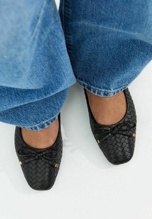 Pies con bailarinas de cuero negro trenzado con pequeños lazos, combinadas con vaqueros azules.