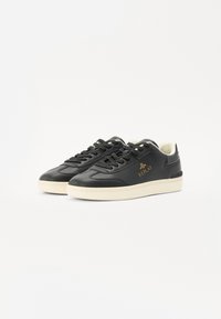 Black leather sneakers with a textured finish, featuring a cream rubber sole, black laces, and gold "REPLAY" logo on the side.