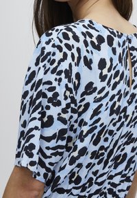 Blå mönstrad topp med leopardtryck i svart och kräm, korta ärmar, mjuk textur och en nyckelhålsöppning på ryggen med en knapp.