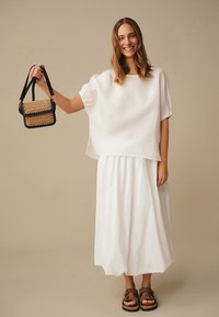 Hvidt hørtop og nederdel med løs pasform. Sort håndtaske med flettede gulddetaljer og brune sandaler fuldender looket.