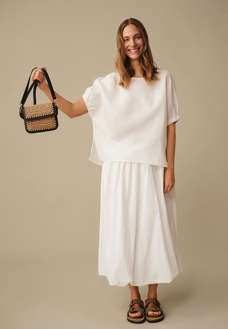 Hvidt hørtop og nederdel med løs pasform. Sort håndtaske med flettede gulddetaljer og brune sandaler fuldender looket.