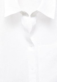 Camisa de lino blanca con un cuello clásico, botones en el frente y un bolsillo de parche en el lado izquierdo. Textura suave con un diseño ligero.