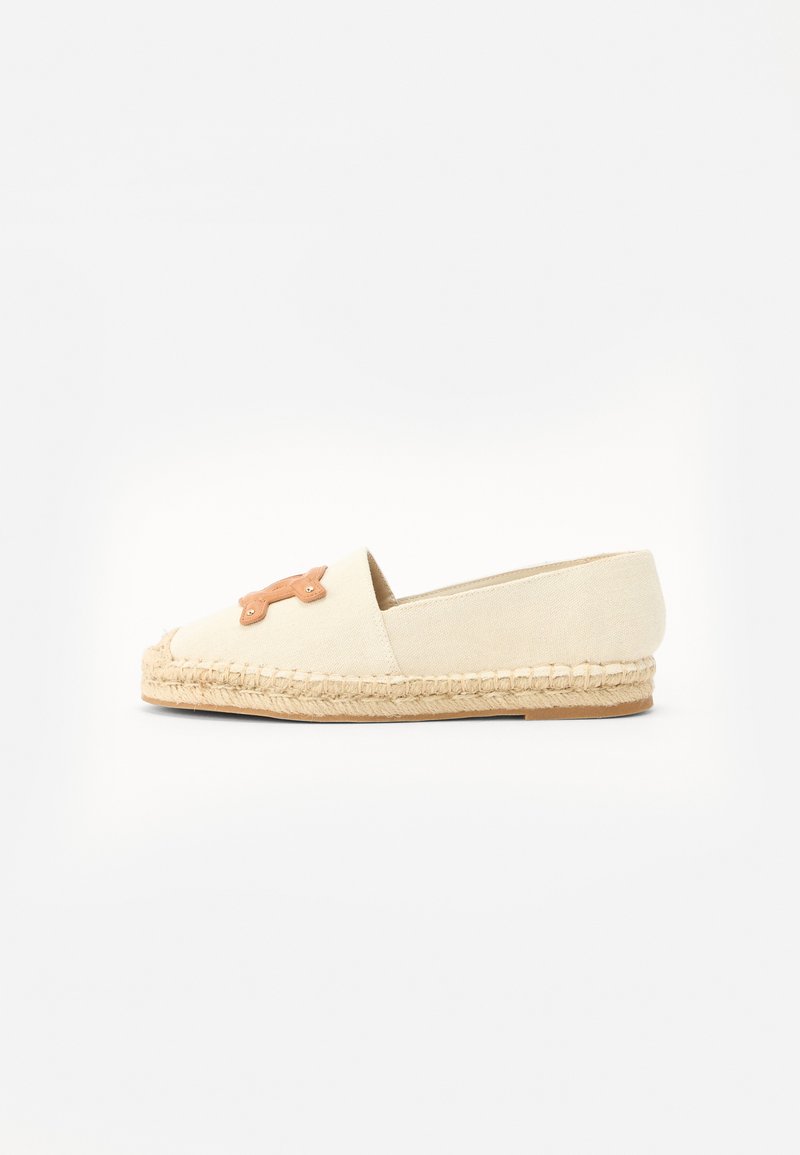 Beige espadrille, jossa on kangas päällinen ja juuttikudospohja. Edessä on koristeellinen ruskea nahka-aksentti. Yksinkertainen ja litteä muotoilu.