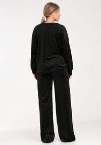 Czarny zestaw odzieży lounge składający się z luźnej bluzki z długim rękawem i spodni o szerokich nogawkach, wykonany z miękkiego, gładkiego materiału o matowym wykończeniu.