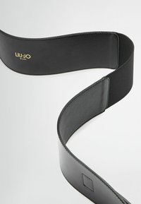 Cintura in pelle nera con texture liscia, dotata di una sezione elastica per il comfort. Logo dorato "LIU-JO MILANO" mostrato in modo prominente.