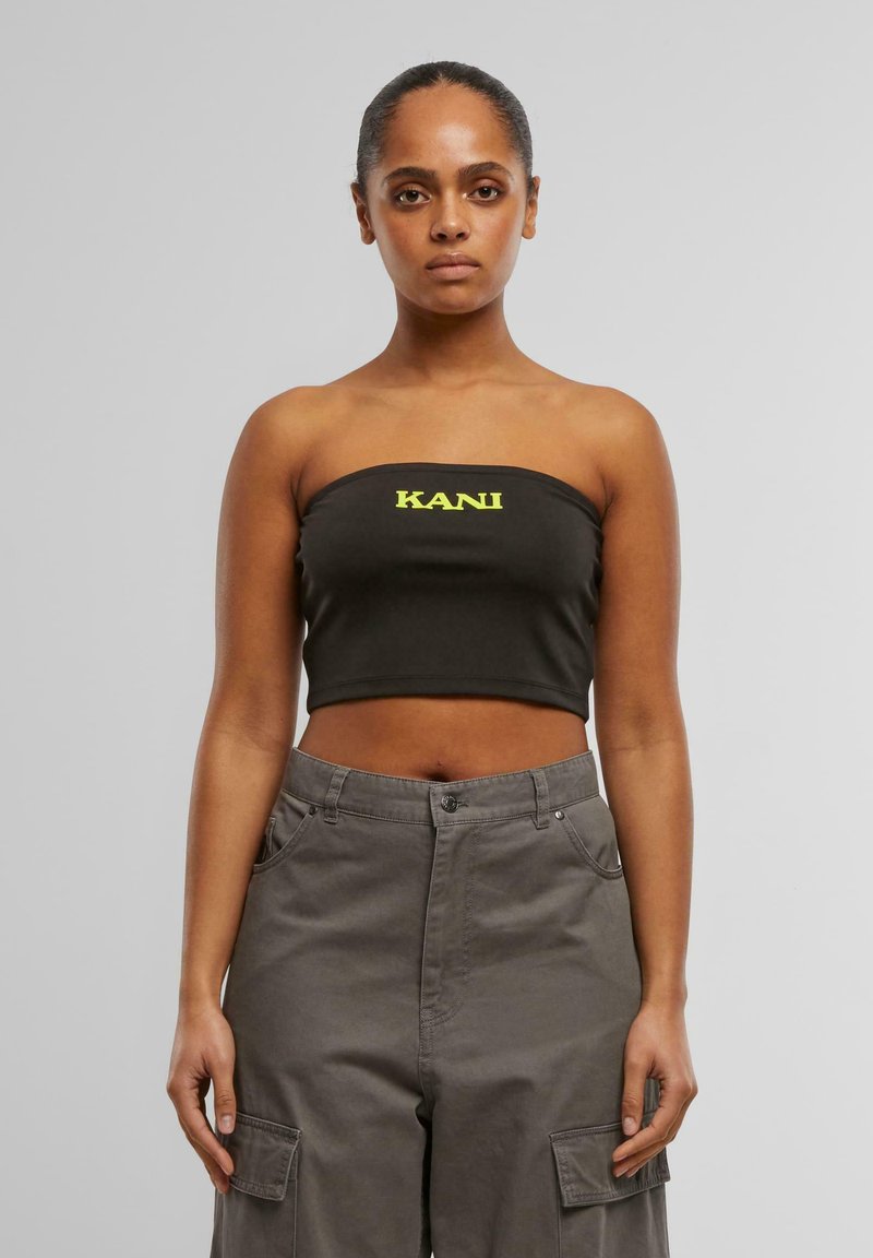 Mustmustamata crop-top musta värviga, millel on erekollased tähed "KANI", paaritatud hallide cargo-pükstega, millel on küljetaskud ja nööbiga sulgimiseks.