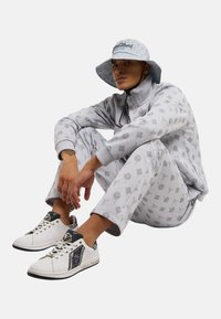 Grå mønstrete genser og bukser, med en matchende bøttehatt. Hvite sneakers har svarte accenter og dekorativ sting.