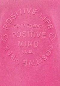 Felpa rosa con testo in rilievo: "VITA POSITIVA", "ENERGIA POSITIVA", "MENTE POSITIVA", circondato da cuori e "CLUB", con una texture liscia.
