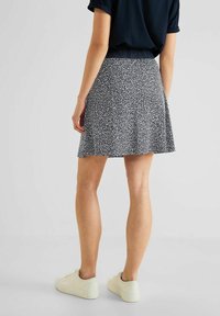 Černobílá sukně se vzorem a rozšířeným tvarem, vyrobená z lehké tkaniny. V kombinaci se světlými teniskami.