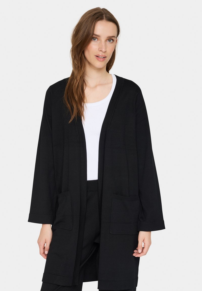 Svart öppen cardigan med mjukt, slätt tyg. Har långa ärmar, två framfickor och en avslappnad passform. Minimalistisk design.