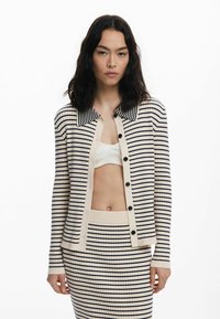 Cardigan crema con righe blu navy, texture a coste e scollatura a colletto. Presenta bottoni frontali e una gonna coordinata a righe.