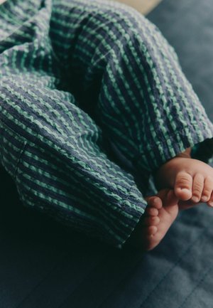 Cotton pajama pants with green and navy vertical stripes, featuring a textured, soft fabric; small toes visible at the bottom.