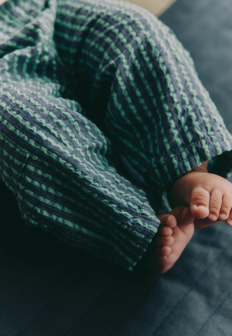 Pantalon de pyjama en coton à rayures verticales vertes et bleues marine, en tissu texturé et doux ; petits orteils visibles en bas.