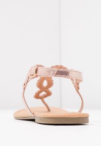 Vaaleanpunaiset metalliset sandaalit koristeellisella hihnalla ja soljella, litteällä pohjalla ja sileällä pinnalla, joissa on huomaamaton kuvio hihnan reunoilla.