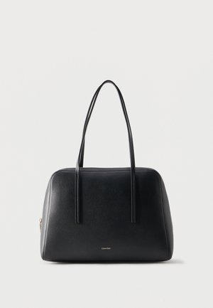 Zwarte leren handtas met twee lange schouderbanden en klein Calvin Klein-logo aan de voorkant, effen lichte achtergrond.