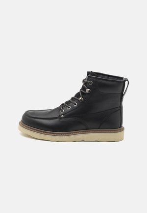 Czarny skórzany botek za kostkę z zaokrąglonym noskiem, szarymi sznurowadłami, pętelką do zakładania, beżową gumową podeszwą oraz subtelnym logo po boku.