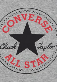 Tissu gris avec un motif circulaire présentant une étoile noire. Texte en rouge indiquant « CONVERSE » et « ALL STAR », avec « Chuck Taylor » en noir.