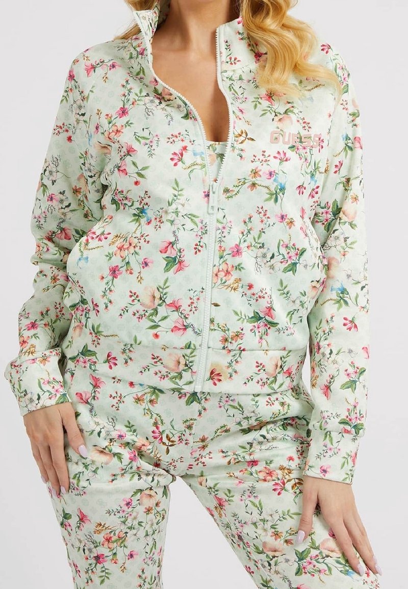 Bloemenspandoek in lichtmintgroen, met een jas met ritssluiting aan de voorkant en bijpassende broek. Versierd met roze en gele bloemen, gladde stof.