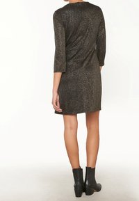 Svart glittrande jerseykjol med trekvartslånga ärmar, en avslappnad passform och rundad halsringning, kombinerad med svarta ankelstövlar.