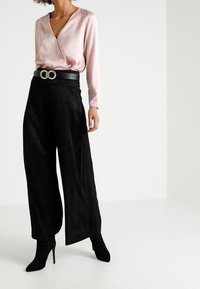 Blouse rose à manches longues, associée à un pantalon noir à jambes larges avec un motif texturé. Ceinture noire avec boucle ronde en accent.