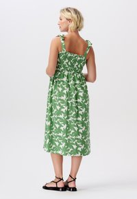 Grön blommig midi-klänning med ett shirrat ryggparti, justerbara band och en avslappnad passform, designad i ett lättviktigt tyg med en mjuk textur.