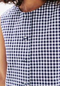 Camicia a quadri navy e bianca con scollo rotondo, senza maniche e dettagli dei bottoni lungo il davanti.