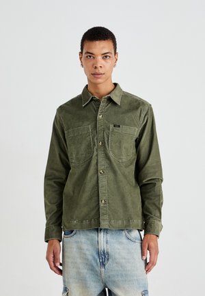 Olive green corduroy shirt with a button-down collar, two chest pockets, and a small brand logo. The fabric has a soft texture.