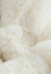 Baltas dirbtinio kailio audinys su pūkuota tekstūra, turintis minkštus, ilgus pluoštus ir subtilų blizgesį, kuriantis jaukią išvaizdą.