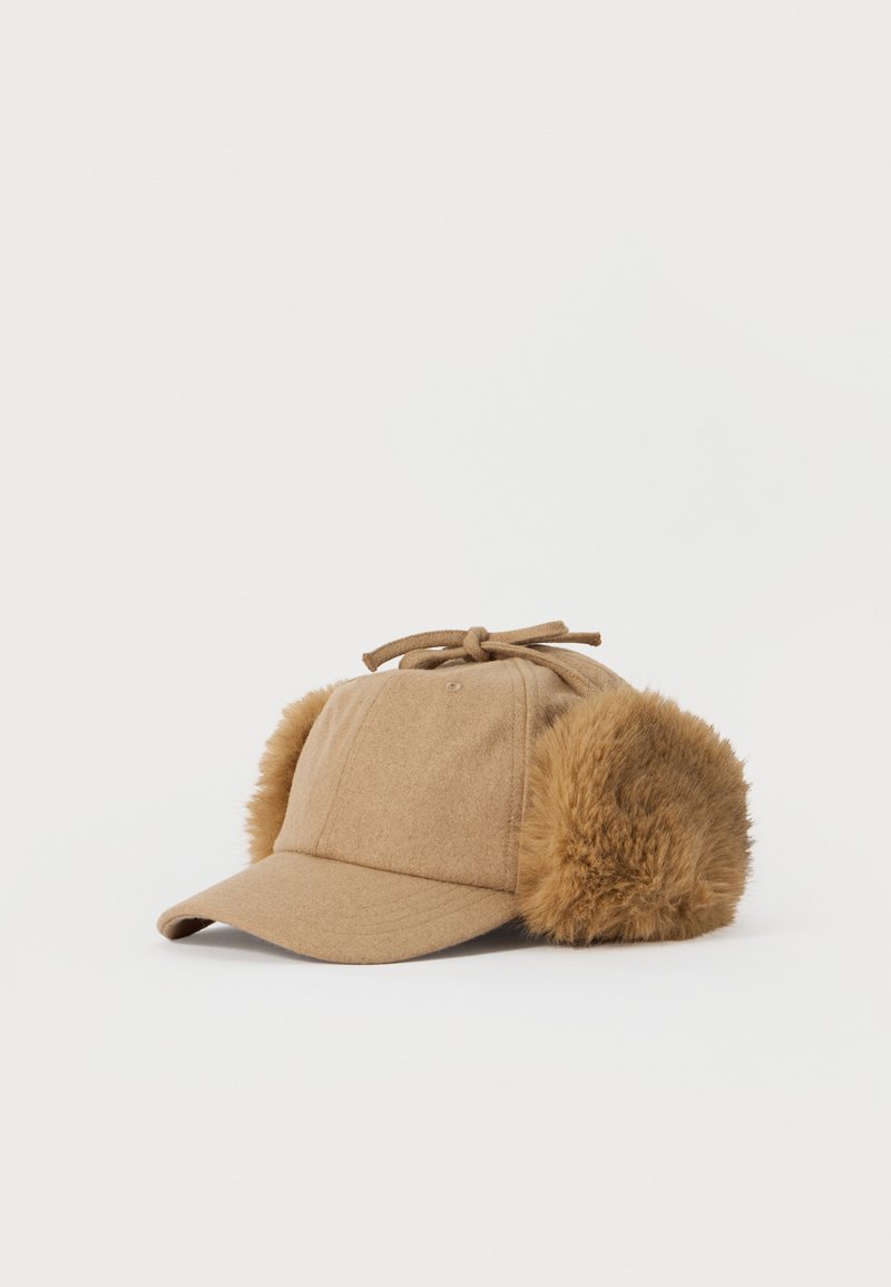 Beige Baseballcap mit angefügten flauschigen Ohrenschützern und einer Bindeschnur auf weißem Hintergrund.