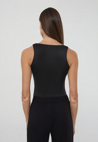Czarny bodysuit o bezrękawowym kroju, gładkiej fakturze i szerokim dekolcie, w połączeniu z czarnymi spodniami, widok od tyłu.