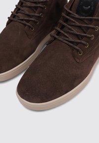 Zapatillas de ante marrón de caña alta con punta redondeada, que presentan cordones redondeados, ojales de metal y una suela de goma texturizada.