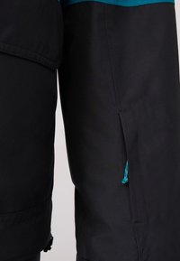 Schwarze wasserfeste Hose mit geradem Schnitt, ausgestattet mit einem türkisfarbenen Akzent an der Taille und einer Zuglasche am Beinausschnitt zur Anpassung.