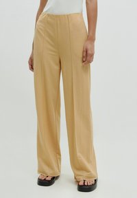 Beige wijde broek van lichtgewicht stof, met voorkanten en een ontspannen pasvorm, gecombineerd met zwarte platform sandalen.