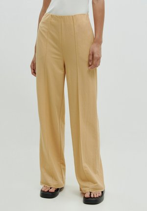 Beige wijde broek van lichtgewicht stof, met voorkanten en een ontspannen pasvorm, gecombineerd met zwarte platform sandalen.