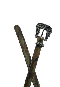 Cinturón de cuero con patrón de camuflaje y hebilla negra con joyas y detalles. Cuenta con dos correas de cinturón cruzadas en el centro.